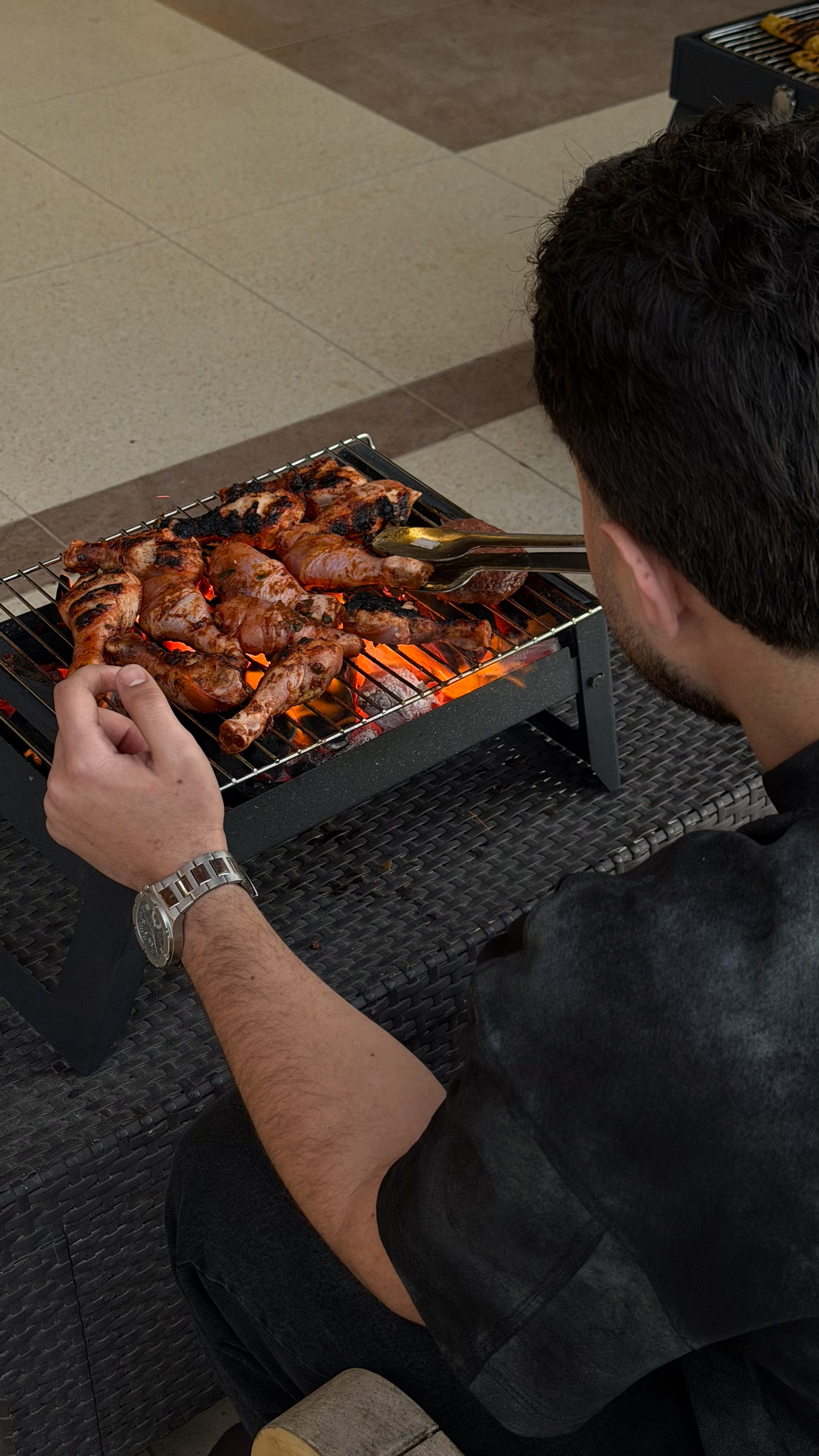 Person grilling chicken on a portable barbecue grill indoors.